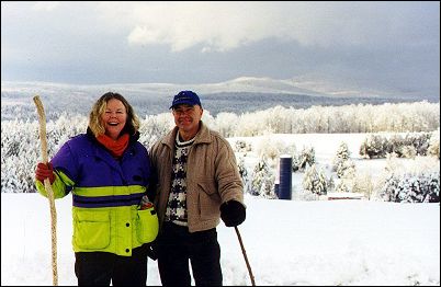 woman and man with walking sticks on hill top with snowy mountains in background